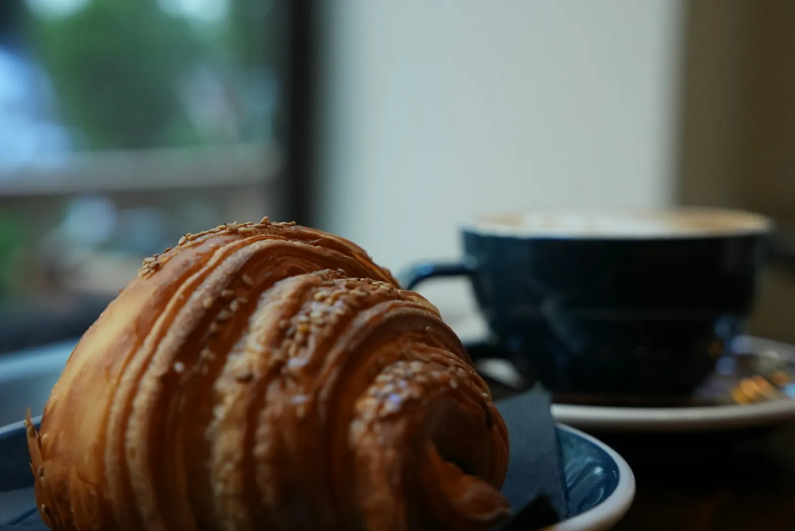 Croissant e xícara de café sobre uma mesa iluminada pelo sol