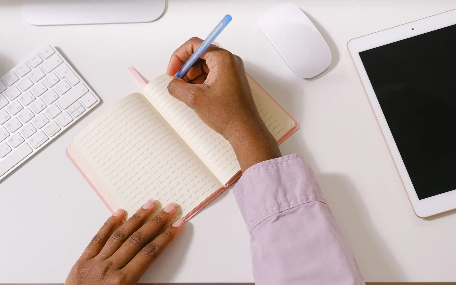 Mãos fazendo anotações em um caderno sobre a mesa.